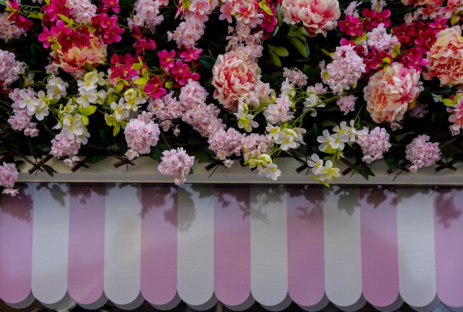 A floral display featuring an arrangement of pink and white hydrangeas, pink Phlox, and white and yellow orchids, placed atop a surface with a pink and white striped awning beneath. The arrangement in